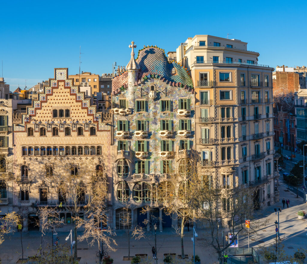 Casa Batlló and neighboring buildings in Barcelona, Spain, with ornate facades and a clear blue sky in the background.