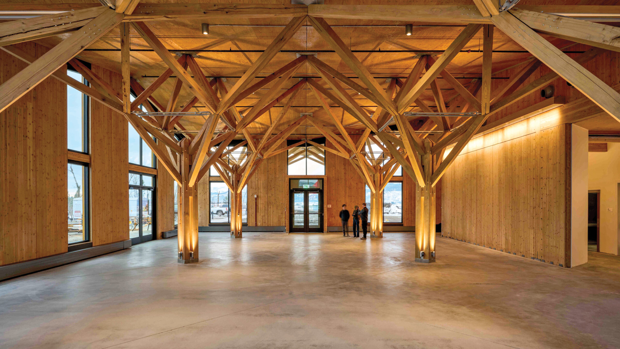 Spacious wooden interior by Leers Weinzapfel Associates with exposed beams, large windows, and a concrete floor; three people stand near the far entrance.