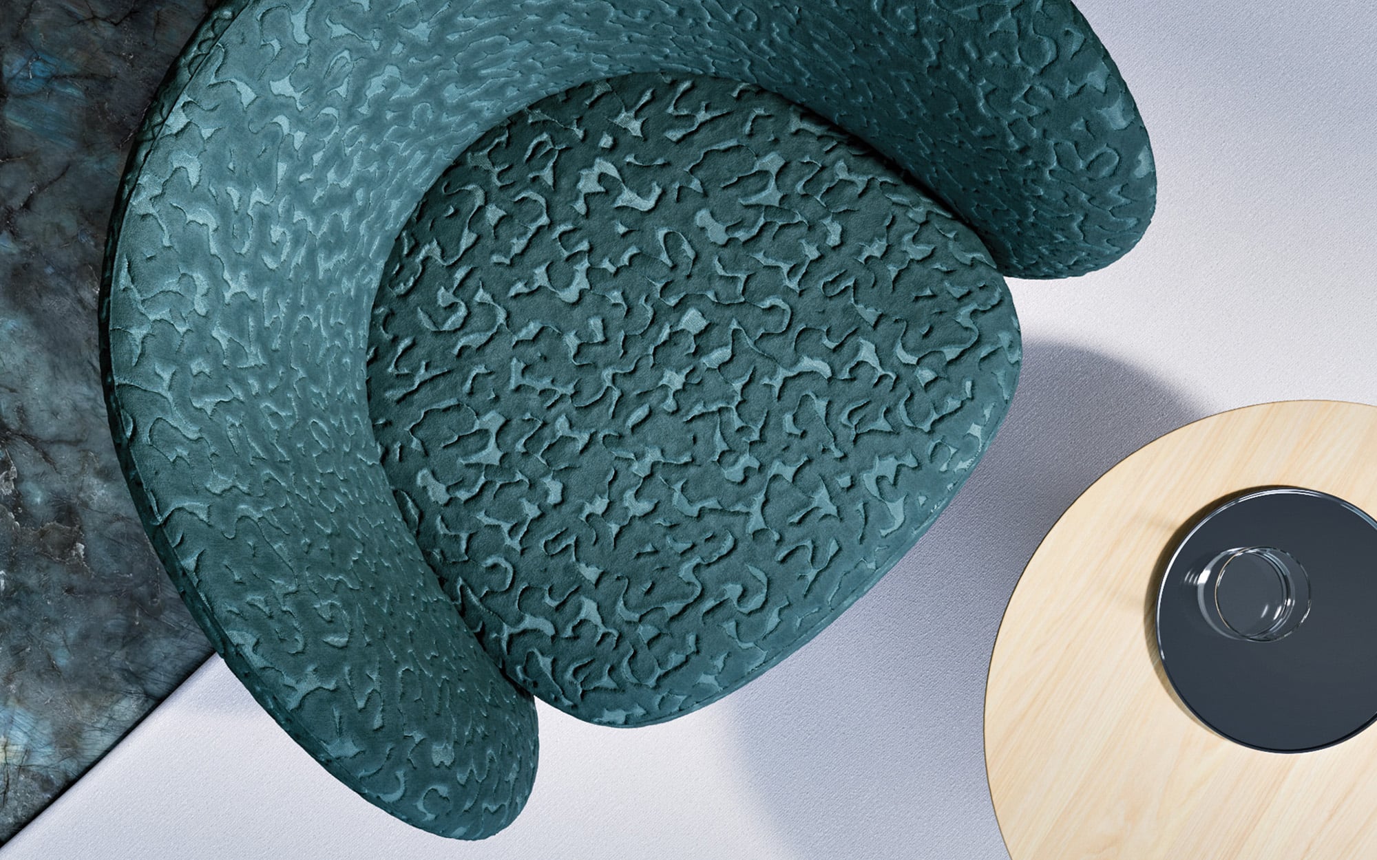Top-down view of a textured green armchair next to a light wooden round table with a black circular item on it, partially visible on a light-colored floor.