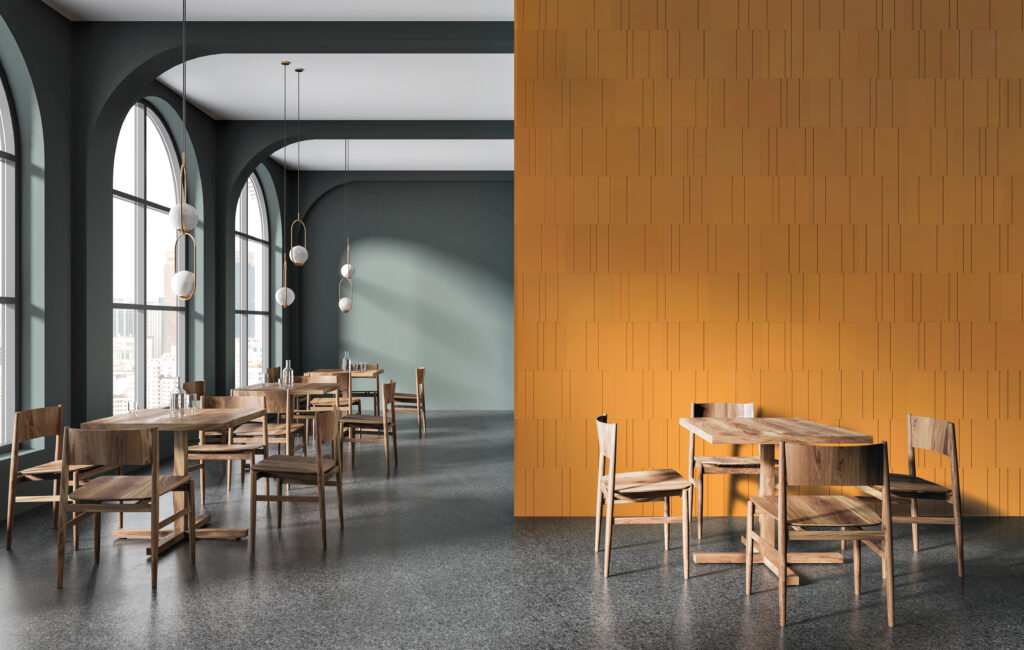 Modern dining area with wooden tables and chairs, large arched windows, gray walls, terrazzo flooring, and a prominent orange tiled accent wall.