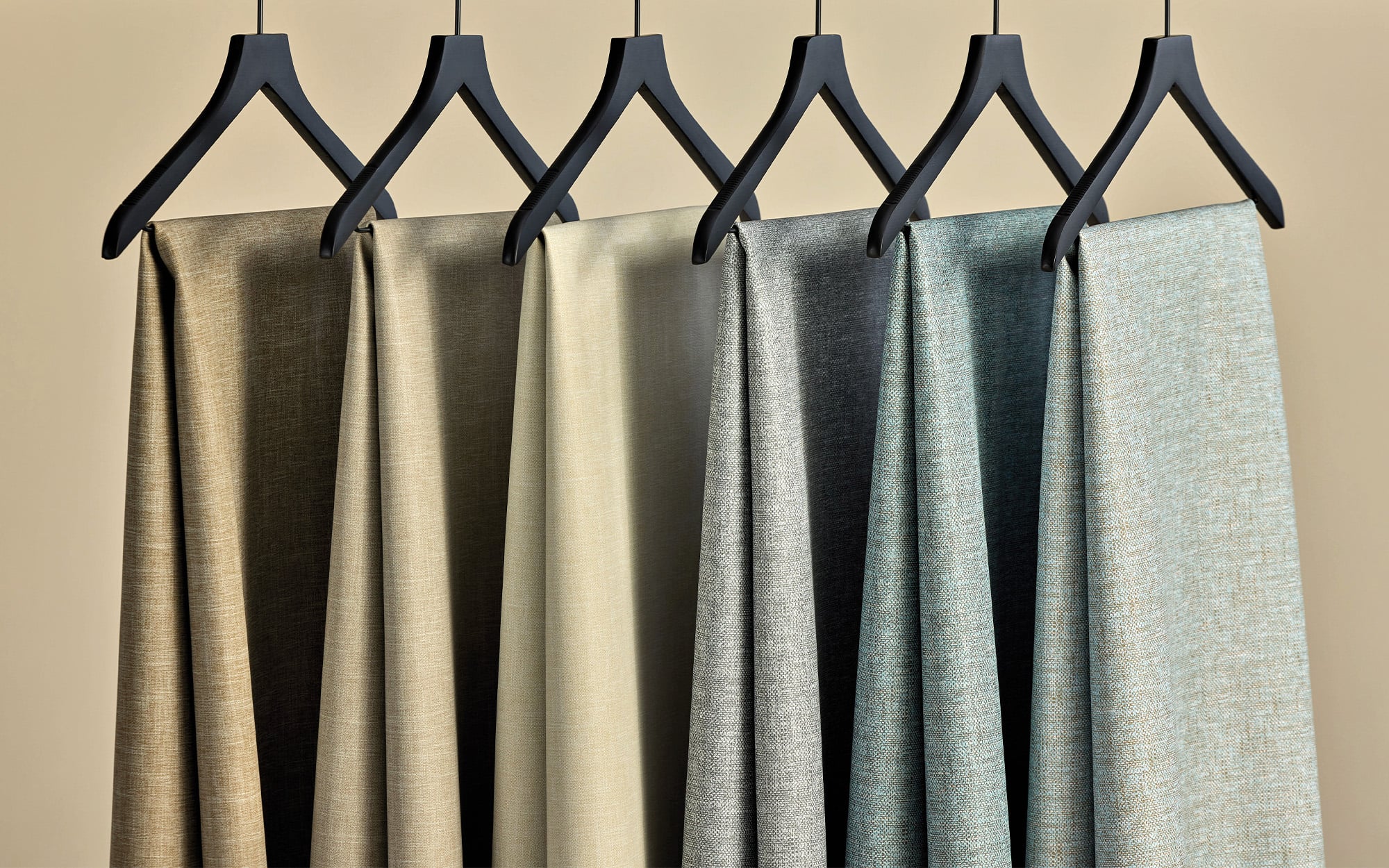 Six fabric swatches in neutral and pastel shades hang on black hangers against a beige background.