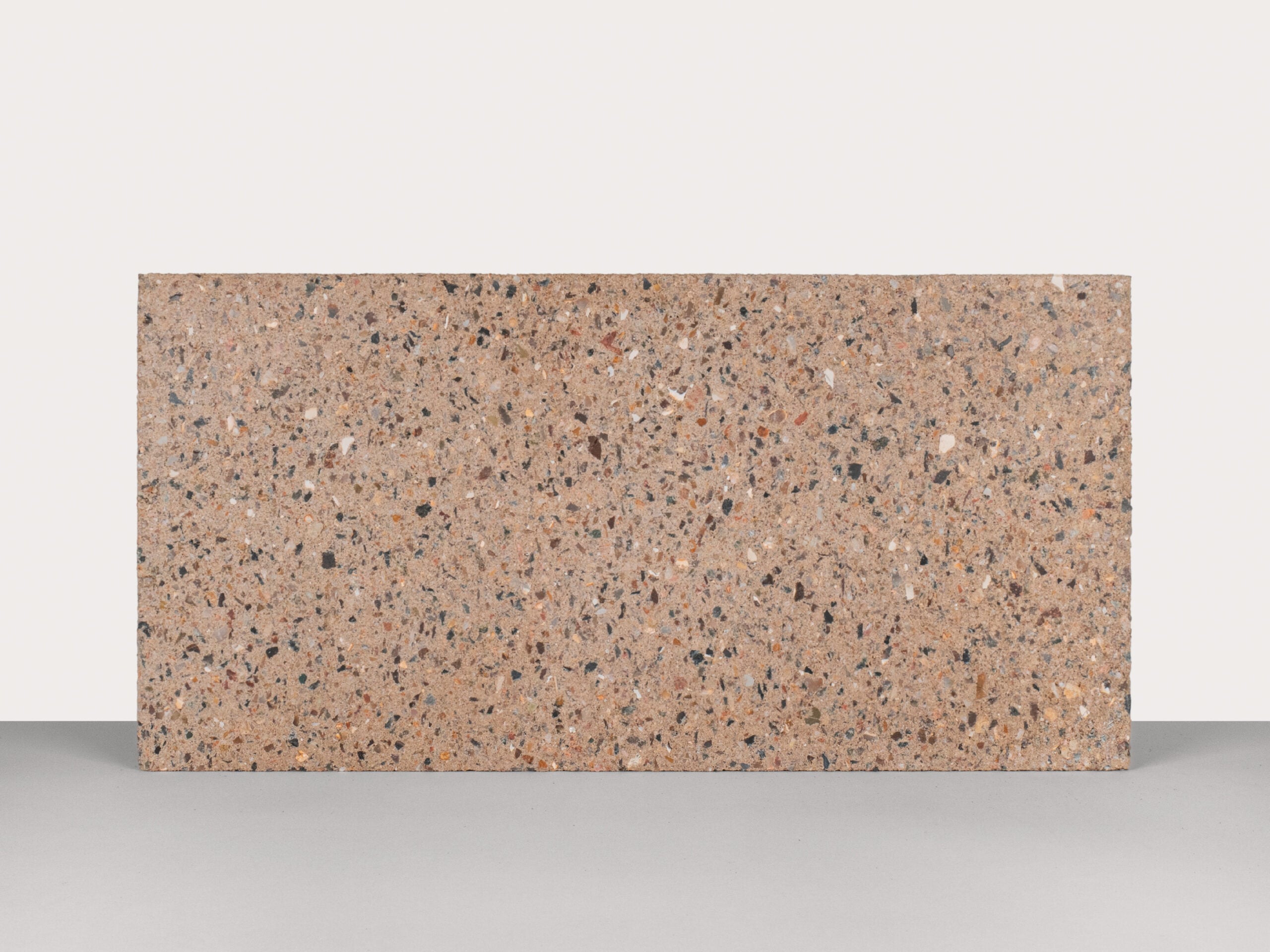 Biobased materials: A rectangular slab of brown terrazzo with multicolored stone chips, standing upright against a plain, light background.