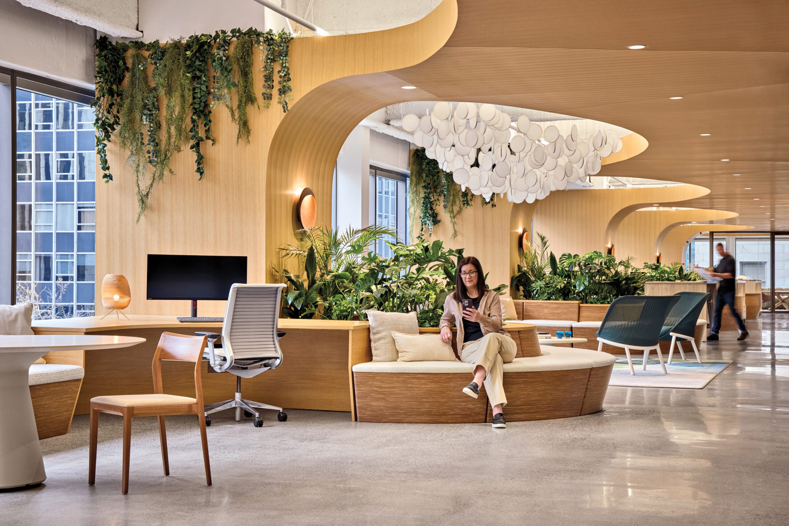 Modern Seattle office space with wooden furnishings, greenery, curved ceiling features, large windows, and people working or relaxing in a bright, open environment.