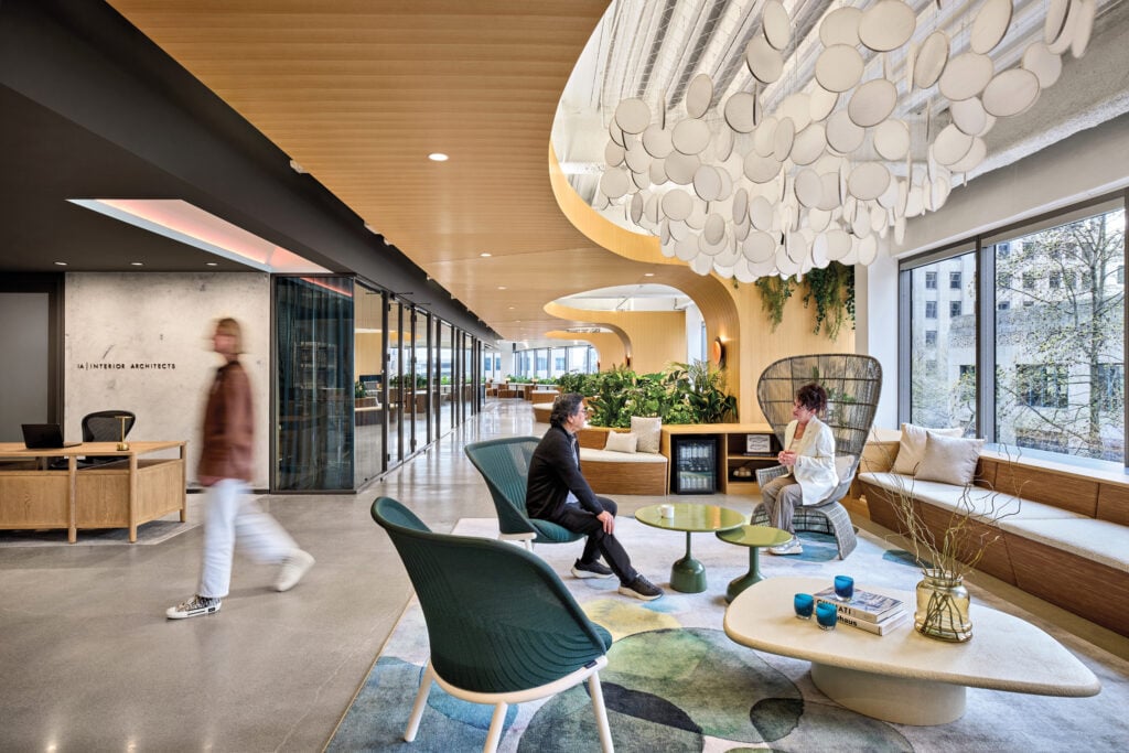 Modern Seattle office lobby with contemporary furniture, large round light fixture, and three people interacting; large windows provide natural light and greenery is visible inside and outside.