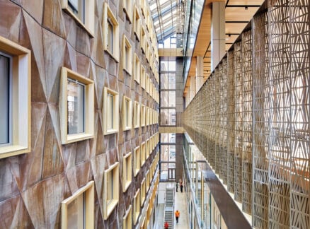 Craft in Architecture: Interior view of a modern building atrium with geometric wall patterns, large windows, a glass ceiling, and people walking along the corridor below.