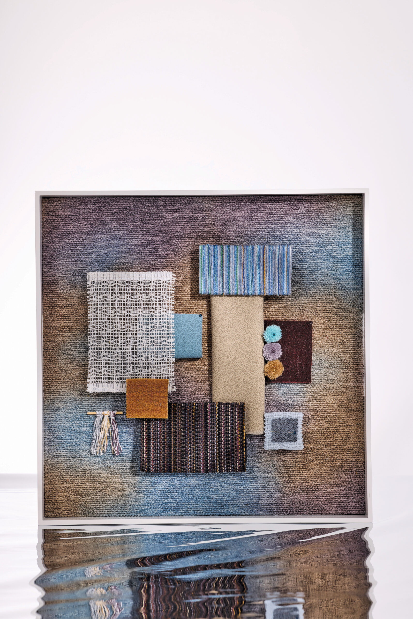 A framed arrangement of assorted fabric and textile samples by Dorothy Cosonas for Luum in various colors and textures is displayed against a gradient background with water reflecting at the bottom.