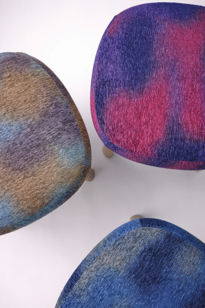 Three square stools with textured upholstery in gradient blue, brown, and purple colors, viewed from above on a white background—an arrangement that's sure to earn METROPOLISLikes for its modern aesthetic.