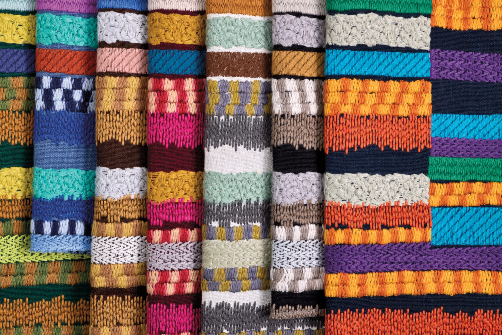 A close-up view of colorful, intricately woven textiles arranged vertically, showcasing various patterns and vibrant horizontal stripes.
