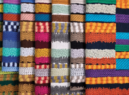 A close-up view of colorful, intricately woven textiles arranged vertically, showcasing various patterns and vibrant horizontal stripes.