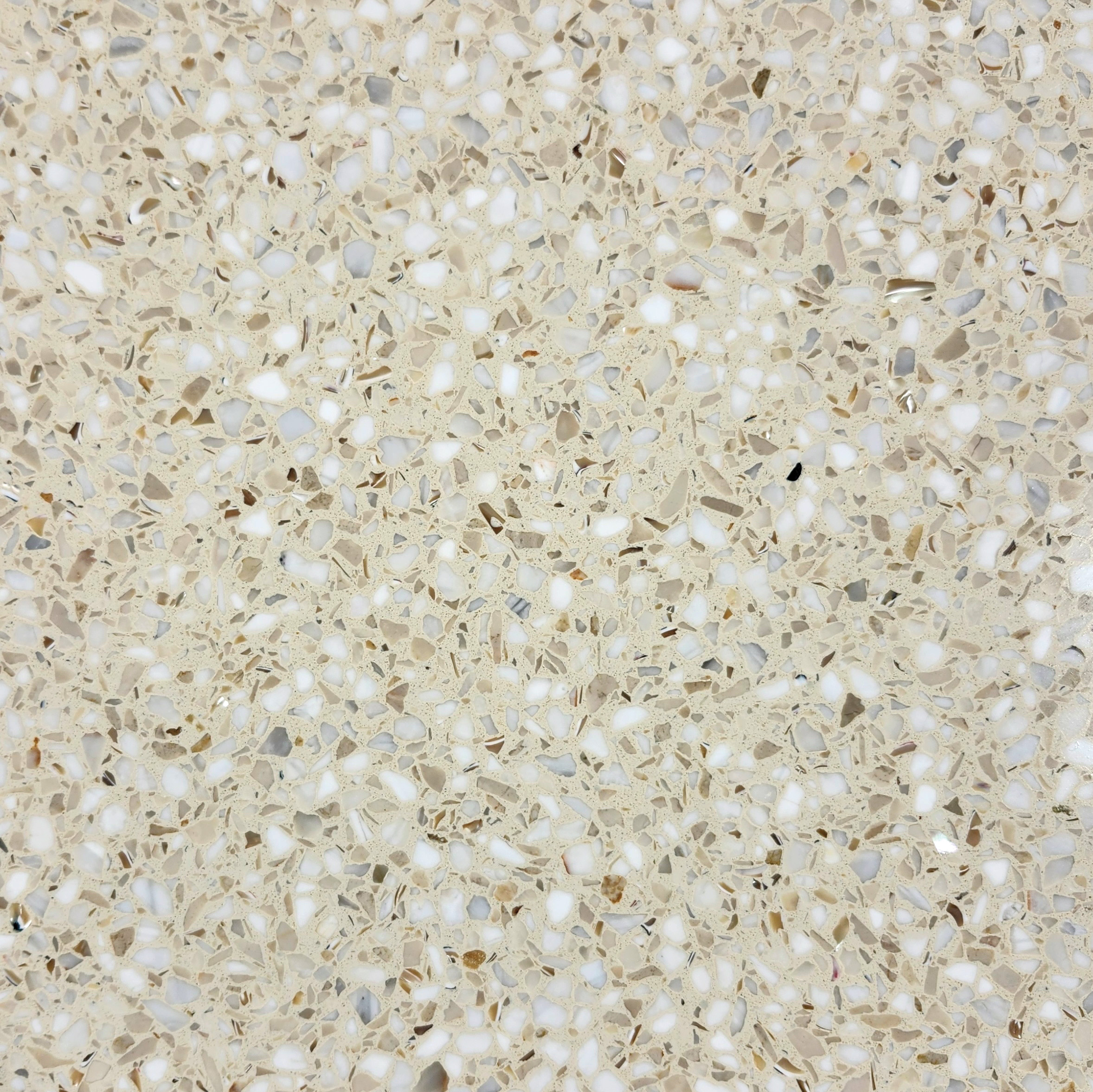 Beige terrazzo surface with scattered white and tan stone chips set in a light-colored matrix.