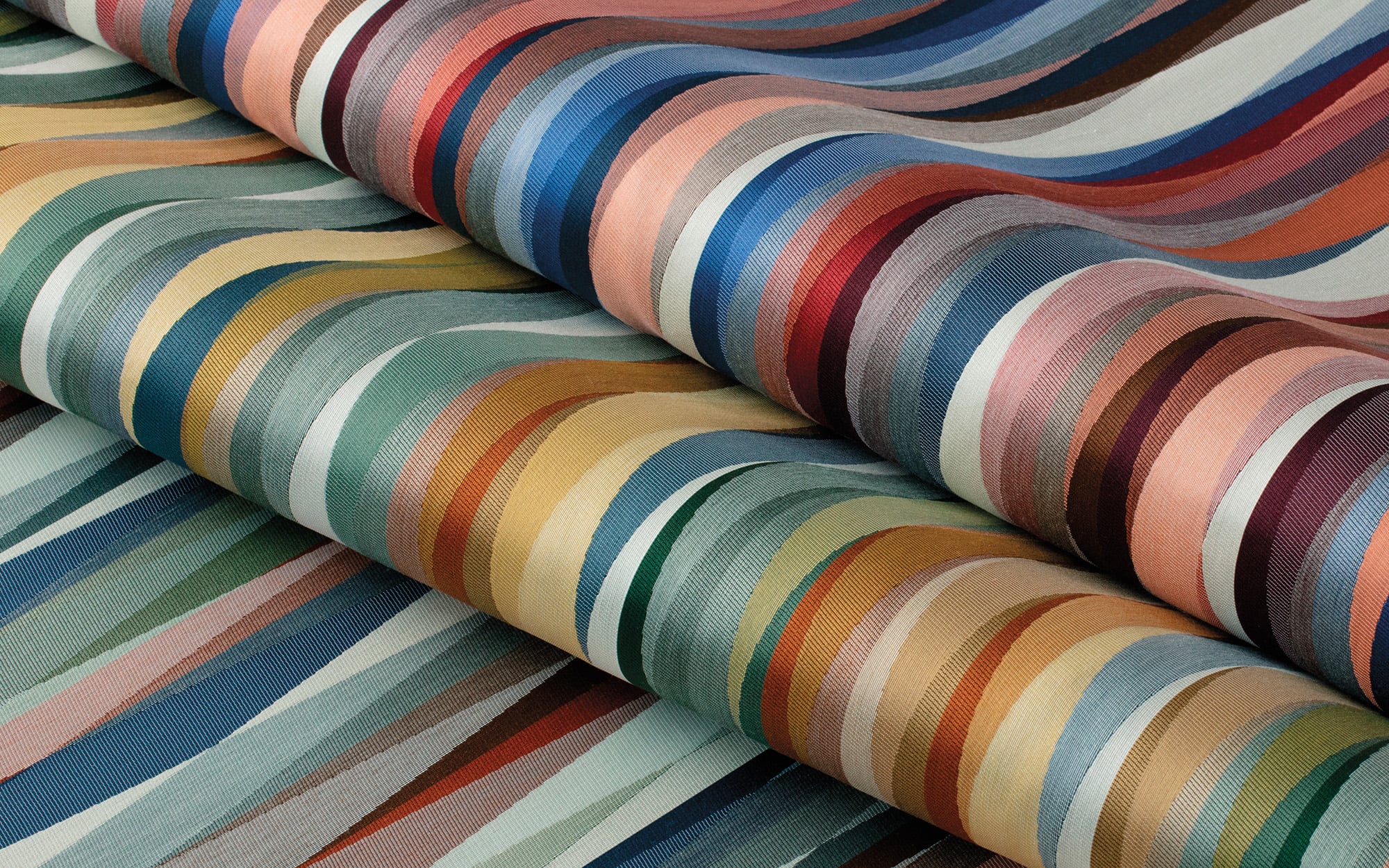 Three rolls of fabric with multicolored, wavy, horizontal stripes in various shades of blue, green, yellow, red, and pink.