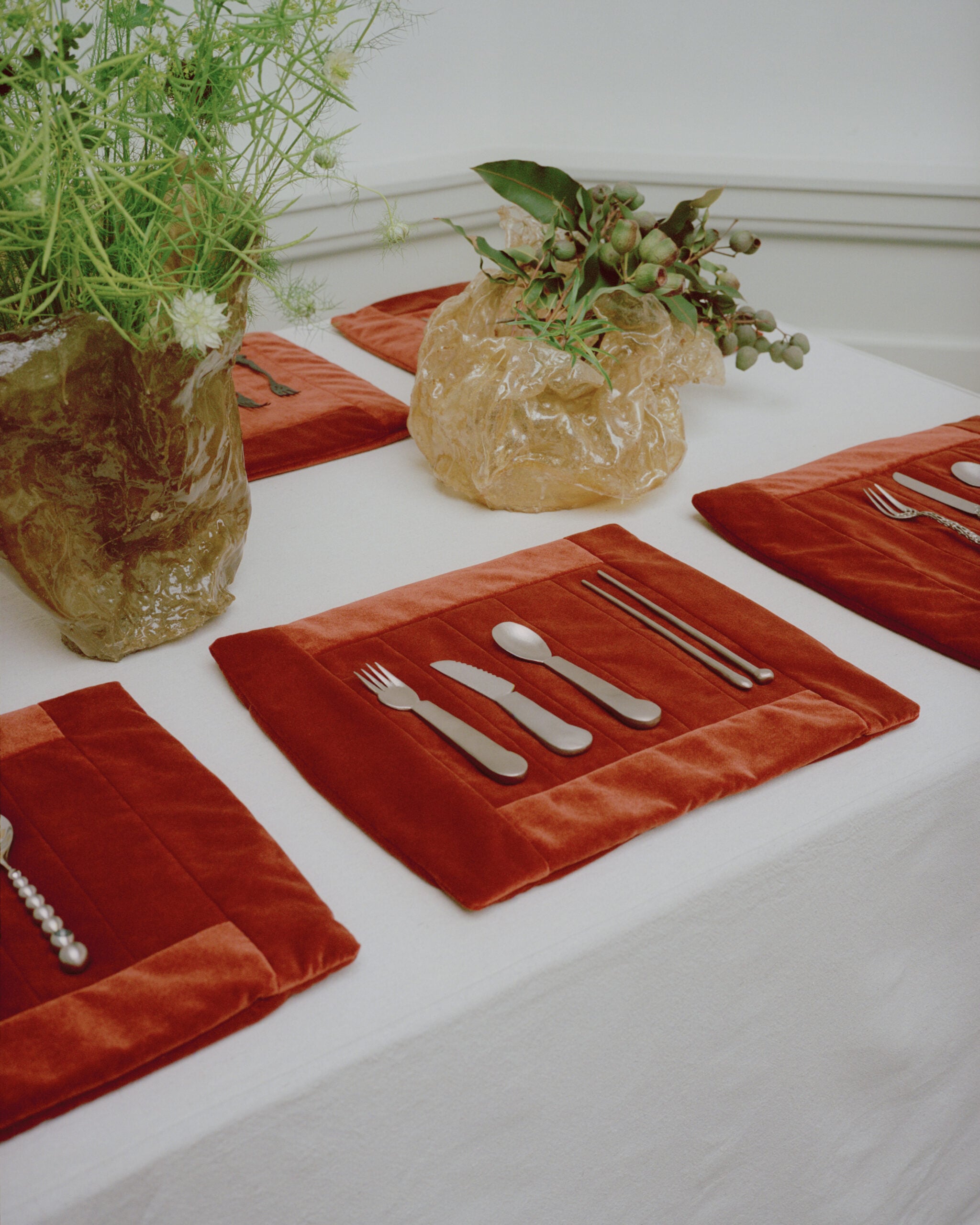 A dining table set with red velvet placemats, silver cutlery, and two vases with green plants on a white tablecloth, inspired by chic trends seen at Milan Design Week 2026.