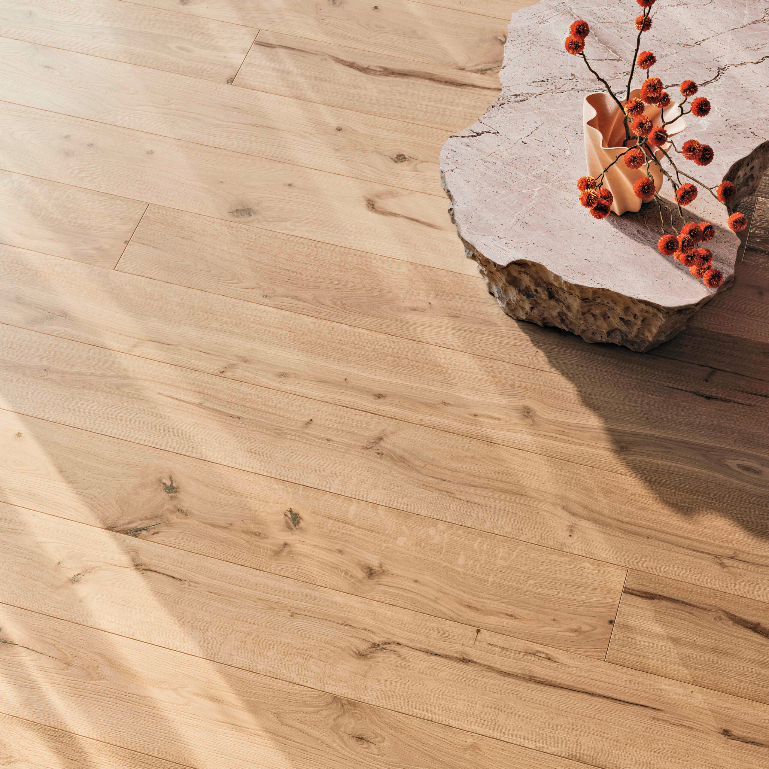 Light wood flooring with natural grain, next to a stone table topped with an orange vase and red-orange berries. Sunlight casts soft shadows across the floor.