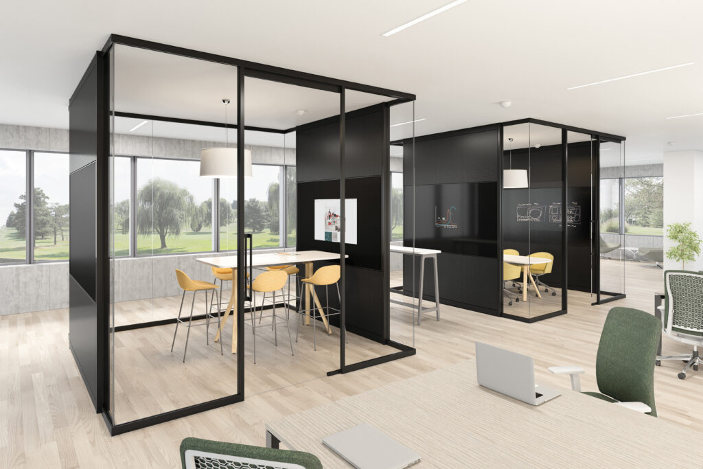 Modern open office space with glass-walled meeting rooms, wooden floors, desks, green chairs, and large windows overlooking trees and a grassy area outside.