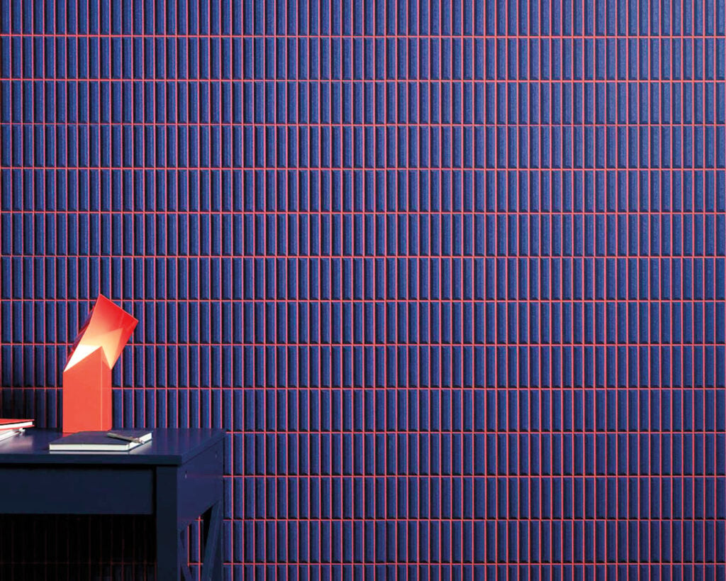 A blue tiled wall with thin red vertical and horizontal lines, next to a blue table holding red geometric decor and a book—METROPOLISLikes this modern, vibrant aesthetic.