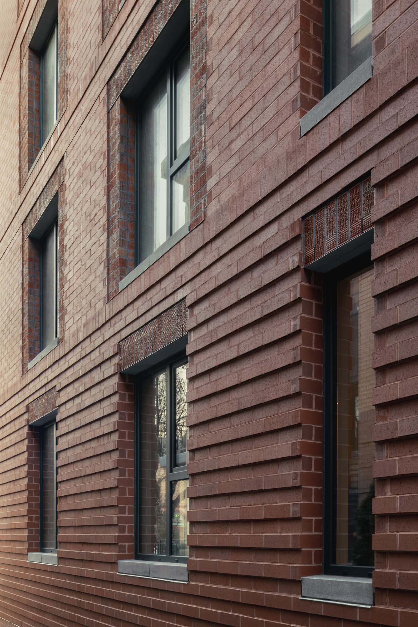 A close-up view of a modern brick building facade with large rectangular windows and horizontal brick detailing.