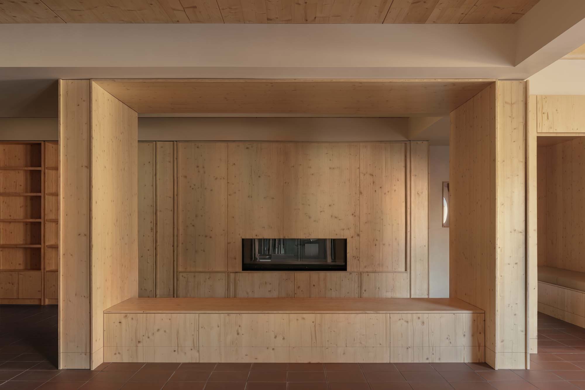 A modern interior with light wood paneling, a built-in bench, and a central fireplace, featuring clean lines and minimalistic design.