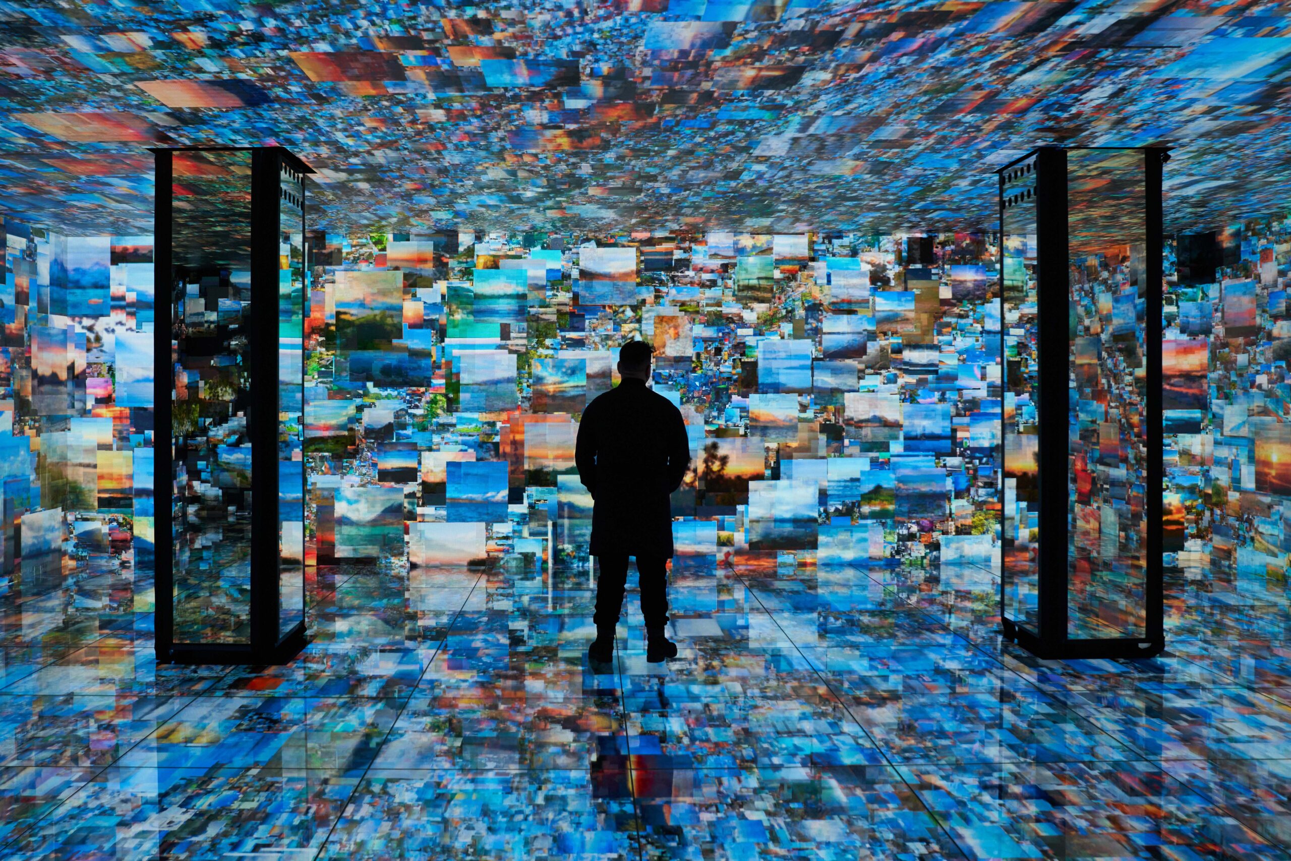 A person stands in a room surrounded by walls, floor, and ceiling covered with digital screens displaying numerous images.