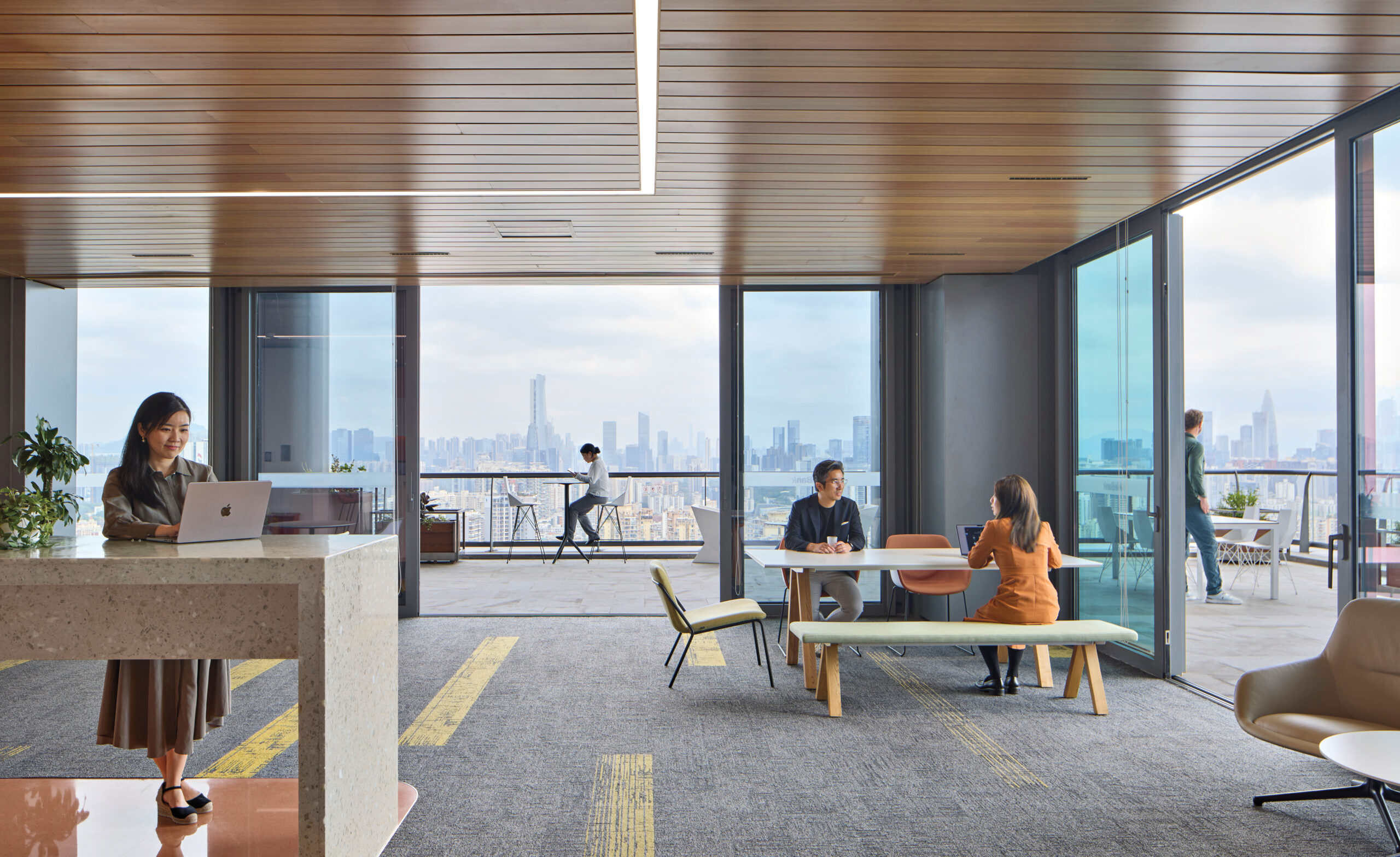 WeBank HQ: Modern office lounge with large windows, people working and meeting at tables, and a city skyline visible in the background.