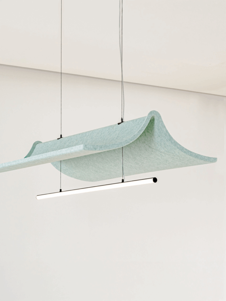 A suspended light fixture hangs below a curved, light green acoustic panel in a minimalist, white room, showcasing modern office products.