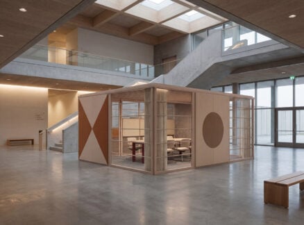 A modern open interior with concrete floors, a central glass and wood meeting cube, a staircase, skylights, minimalist furnishings, and sleek office products for an elevated workspace.