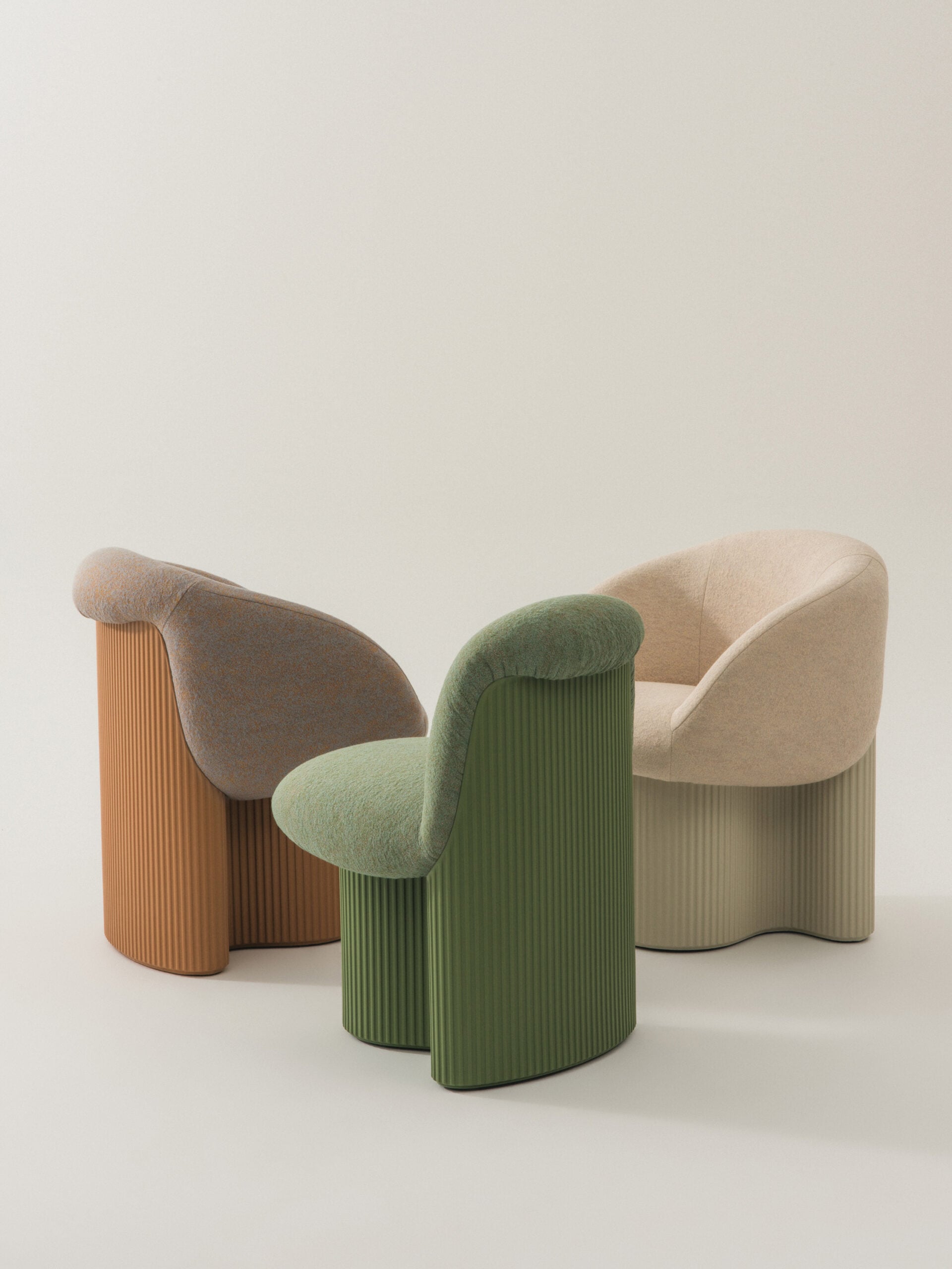 Three upholstered chairs by Andreu World with ribbed bases in brown, green, and beige are arranged in a semi-circle on a light, plain background.