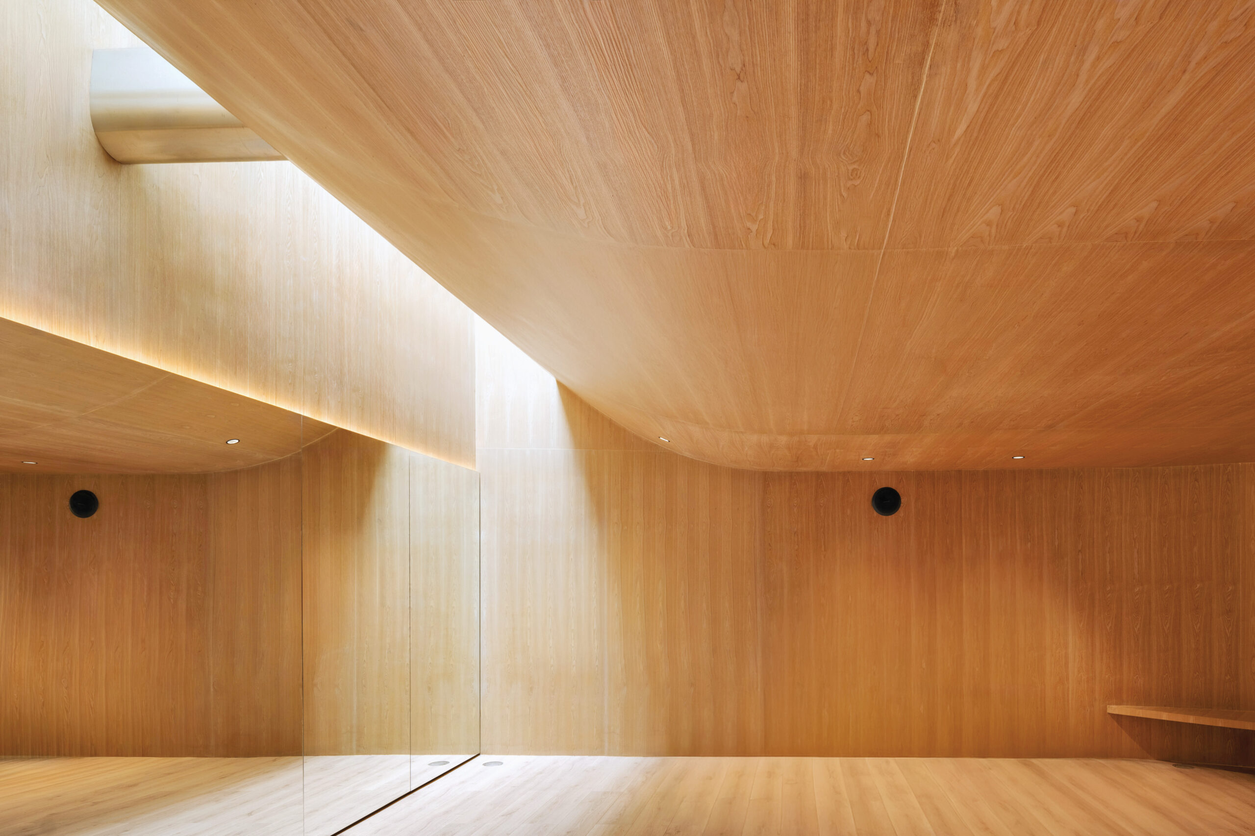 Minimalist interior space featuring light wood walls, ceiling, and floor, with natural light entering through a skylight and reflected off a large mirror—a refined aesthetic reminiscent of Neri&Hu’s signature style.