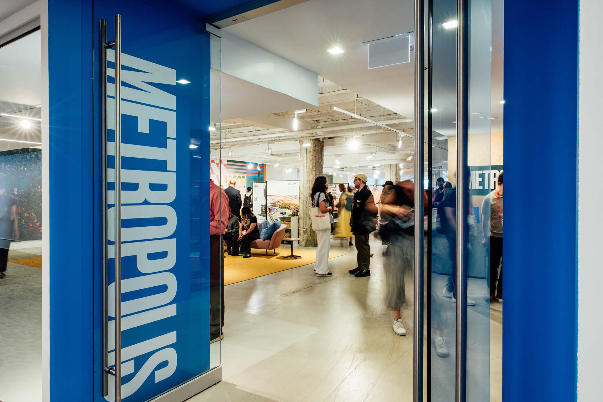People gather and converse inside a modern, brightly lit space, viewed through open glass doors adorned with "METROPOLIS Sustainability Lab" signage.
