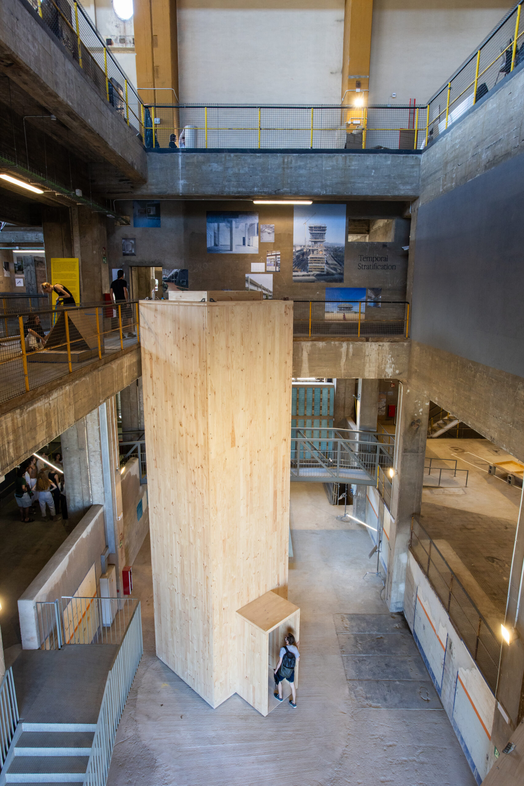 A person stands at the entrance of a tall, wooden structure inside an industrial-style building with concrete walls and multiple levels during 3daysofdesign.