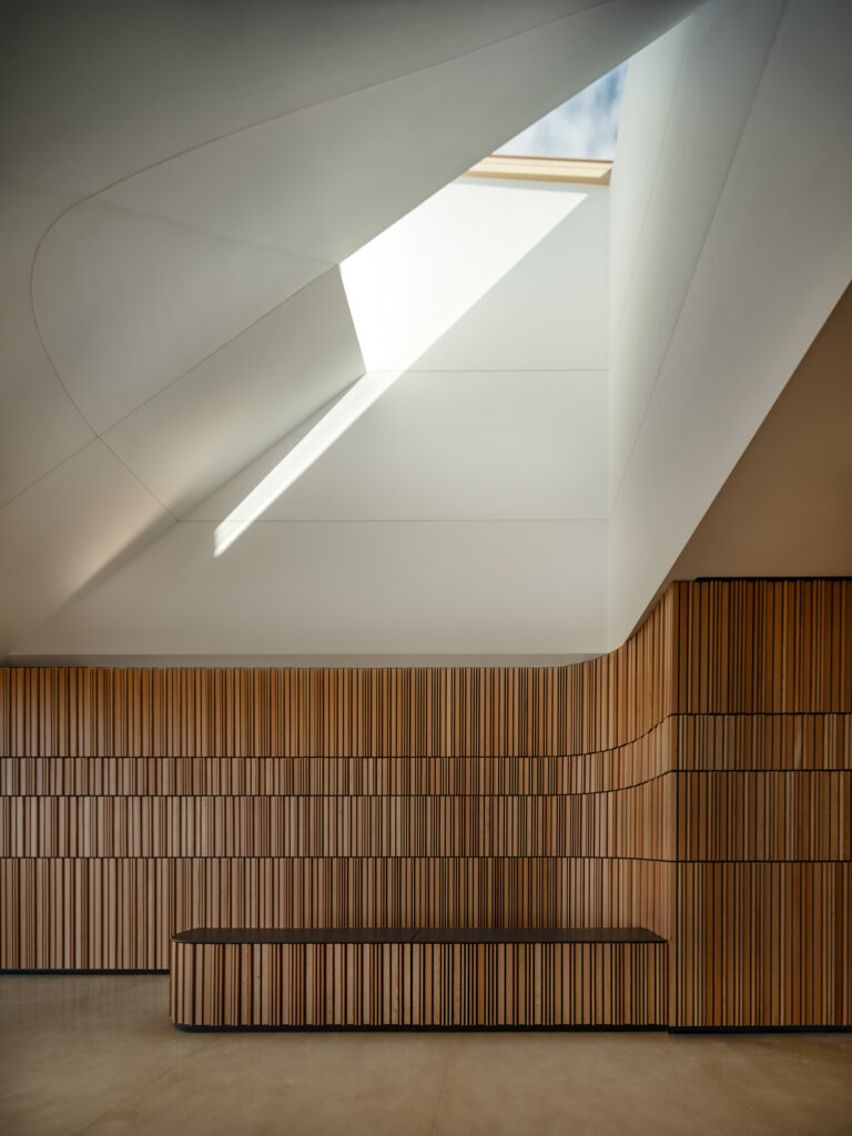 Modern interior with wooden paneling, a minimalist bench, and a large angular skylight allowing natural light into the space—an inviting setting inspired by the Theodore Roosevelt Presidential Library’s design ethos.