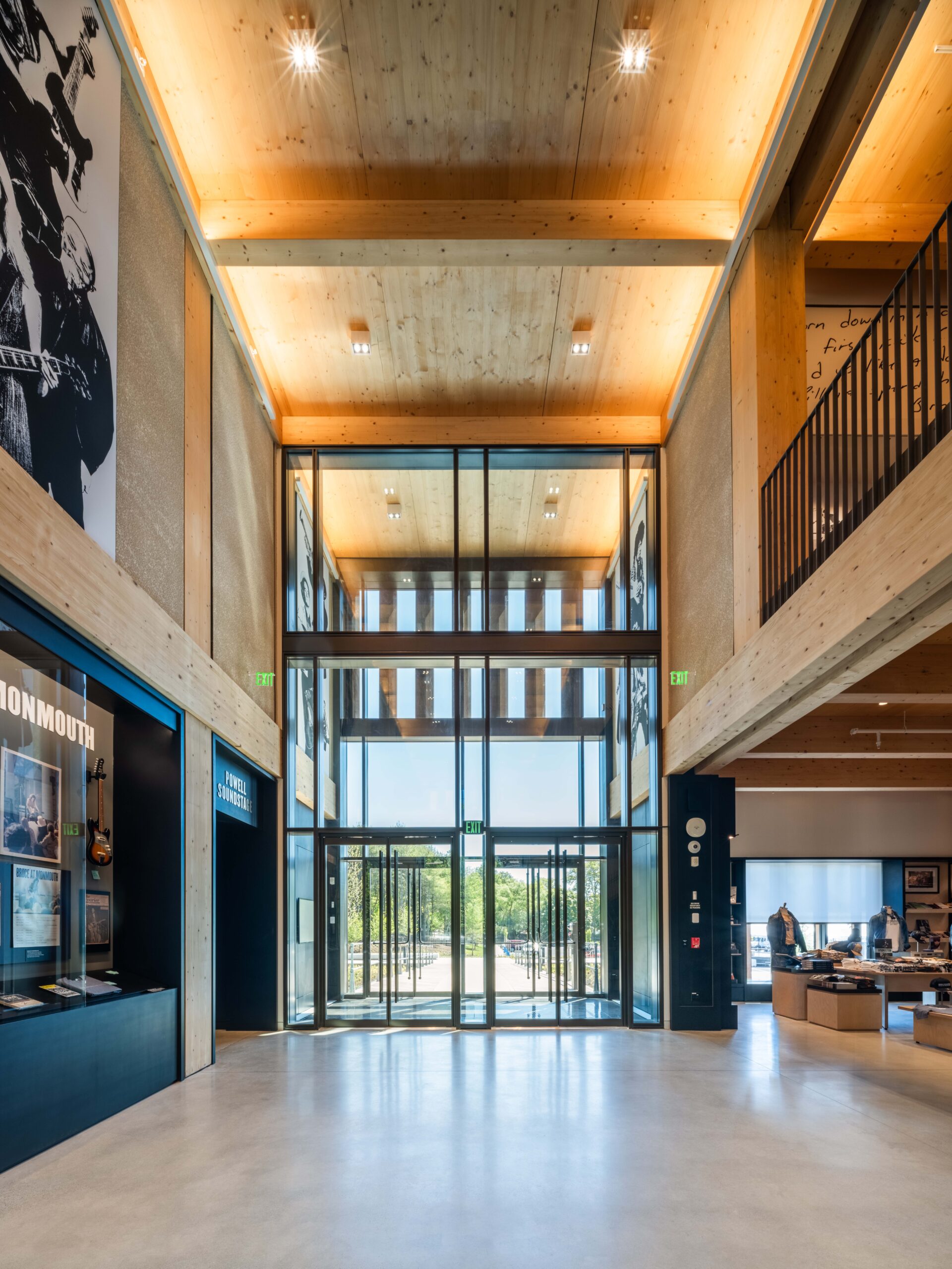 Spacious modern lobby with high wooden ceilings, large glass entry doors, display area on the left, and a reception desk on the right. Natural light fills the space.
