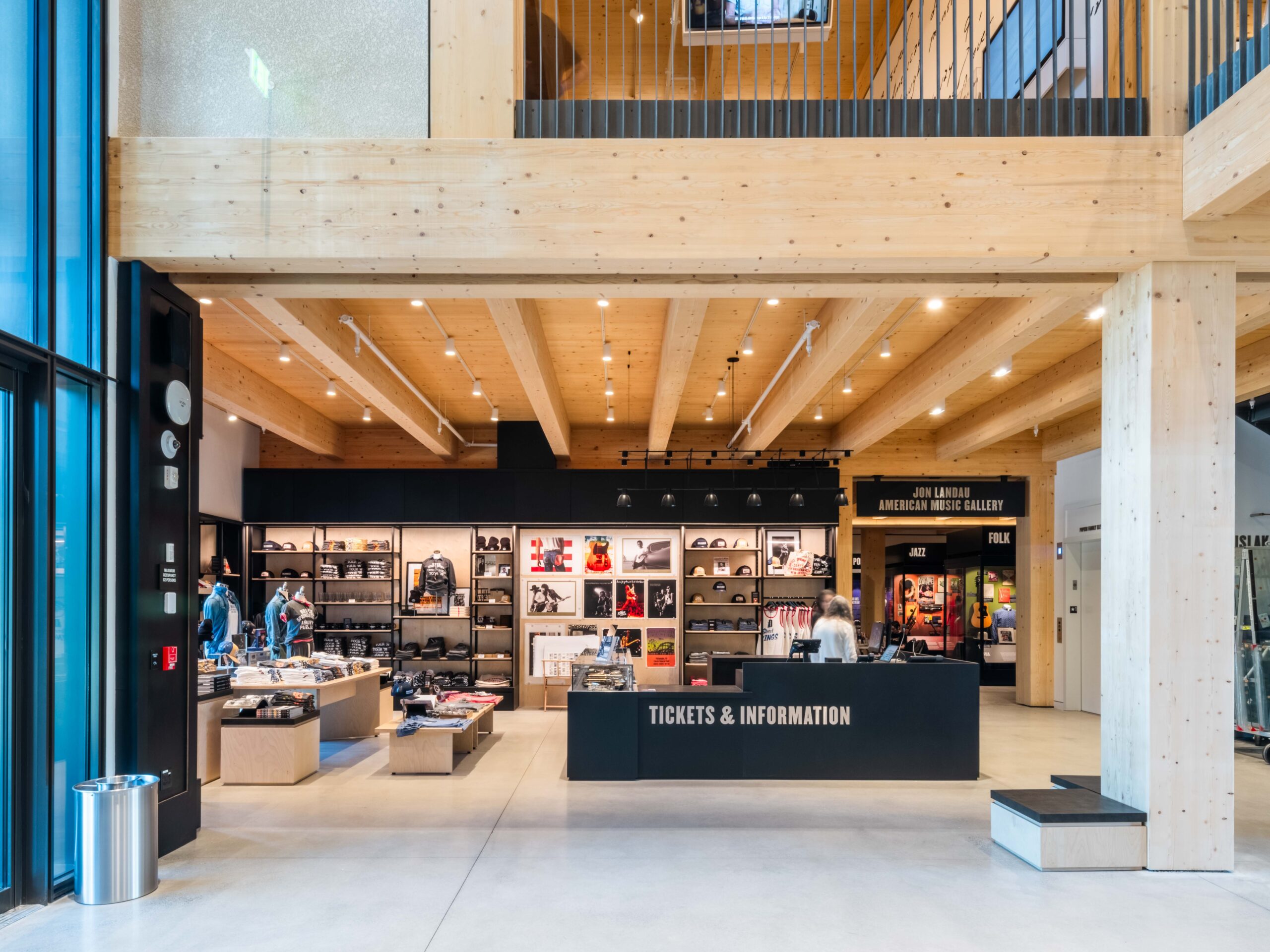 Modern ticket and information desk inside a spacious building with wooden beams, retail shelves, and merchandise displays.