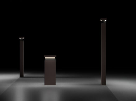 Neuro-Inclusive Lighting Solutions: Three dark rectangular pillars of varying heights stand on a smooth, dimly lit surface with small lights atop each, against a black background.