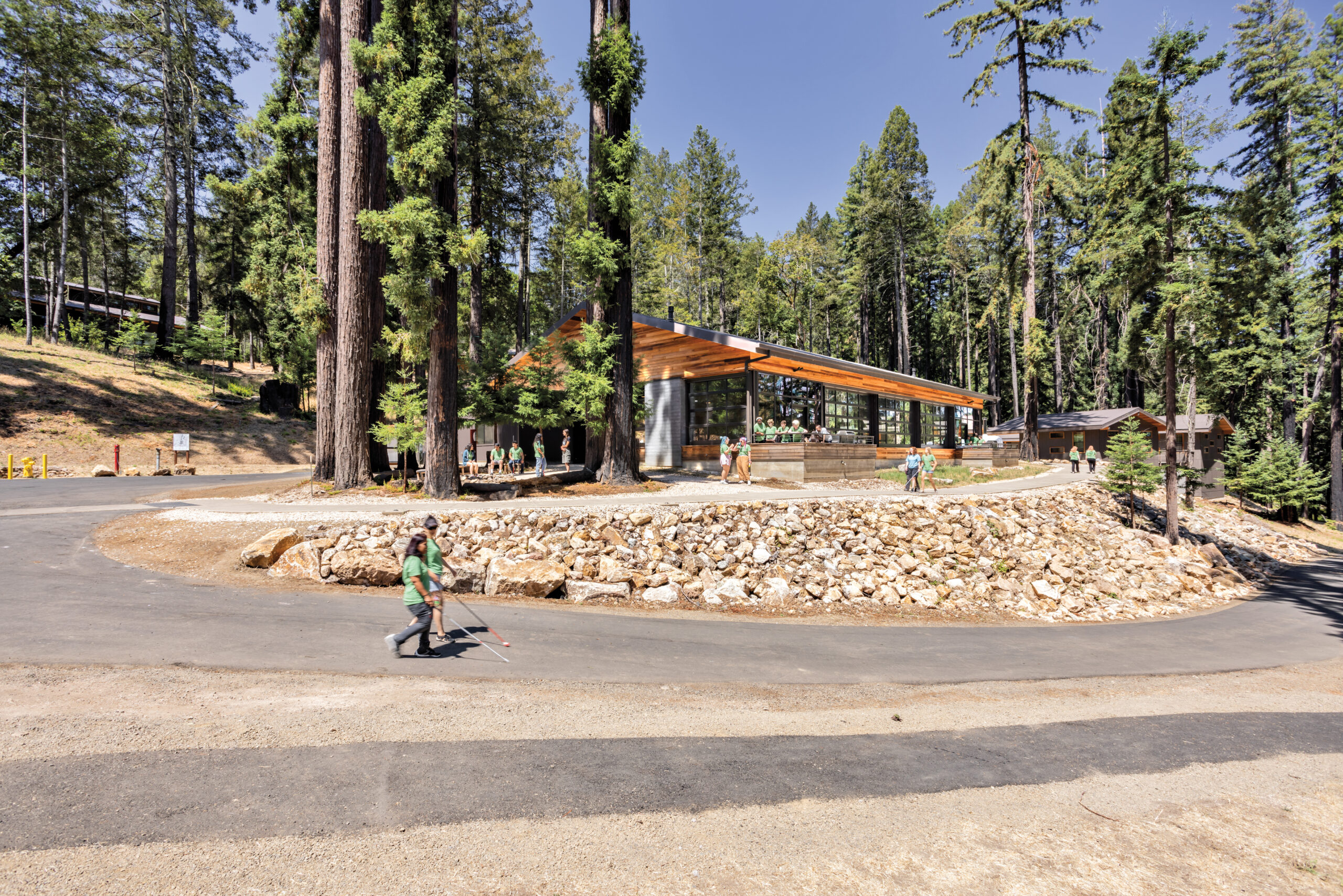 At a camp for the blind, a wood structure sits in a forested area with people using white canes.