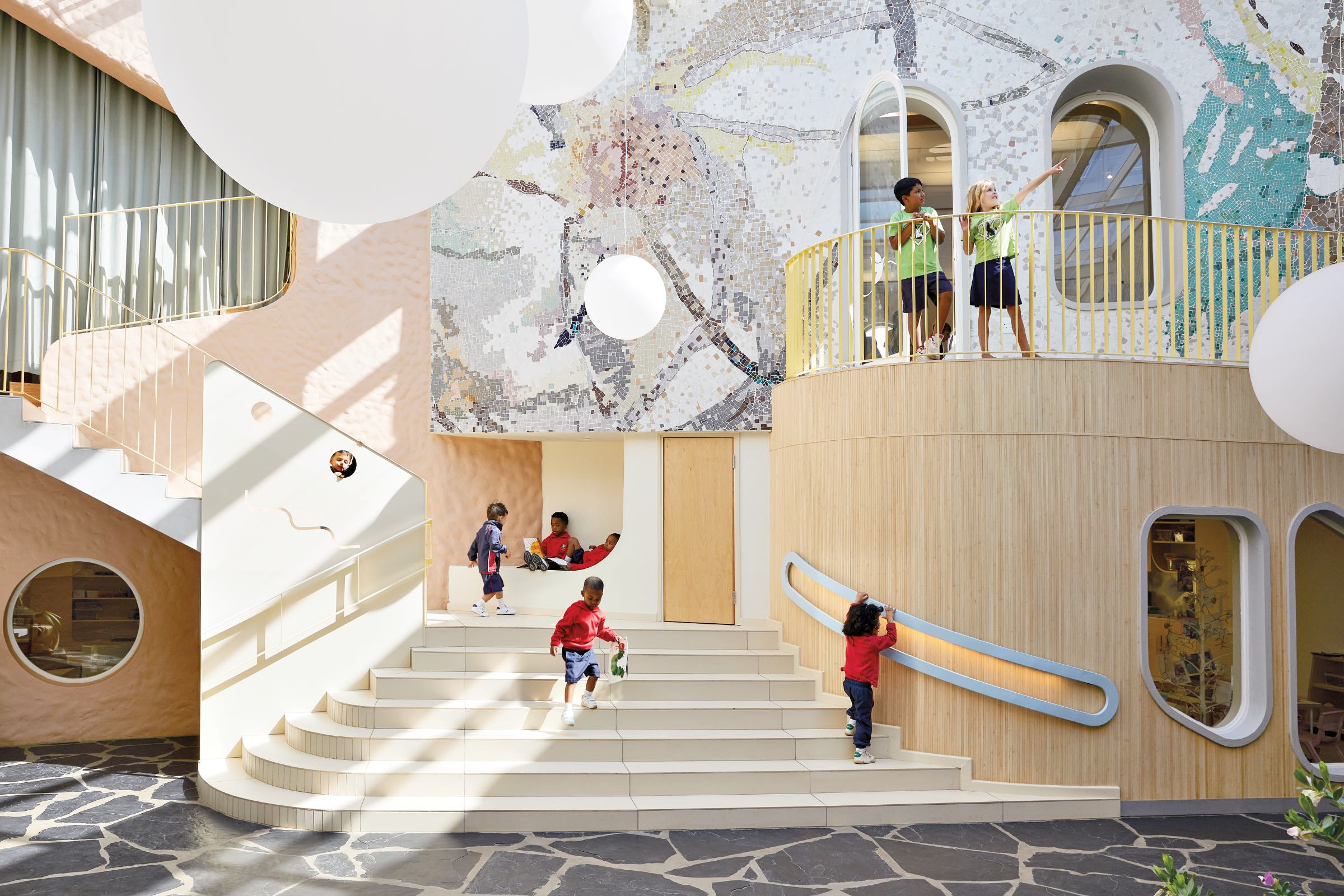 Hubo Studio: Children play and interact on white steps and balconies inside a colorful, modern building with large round windows and mosaic wall art.