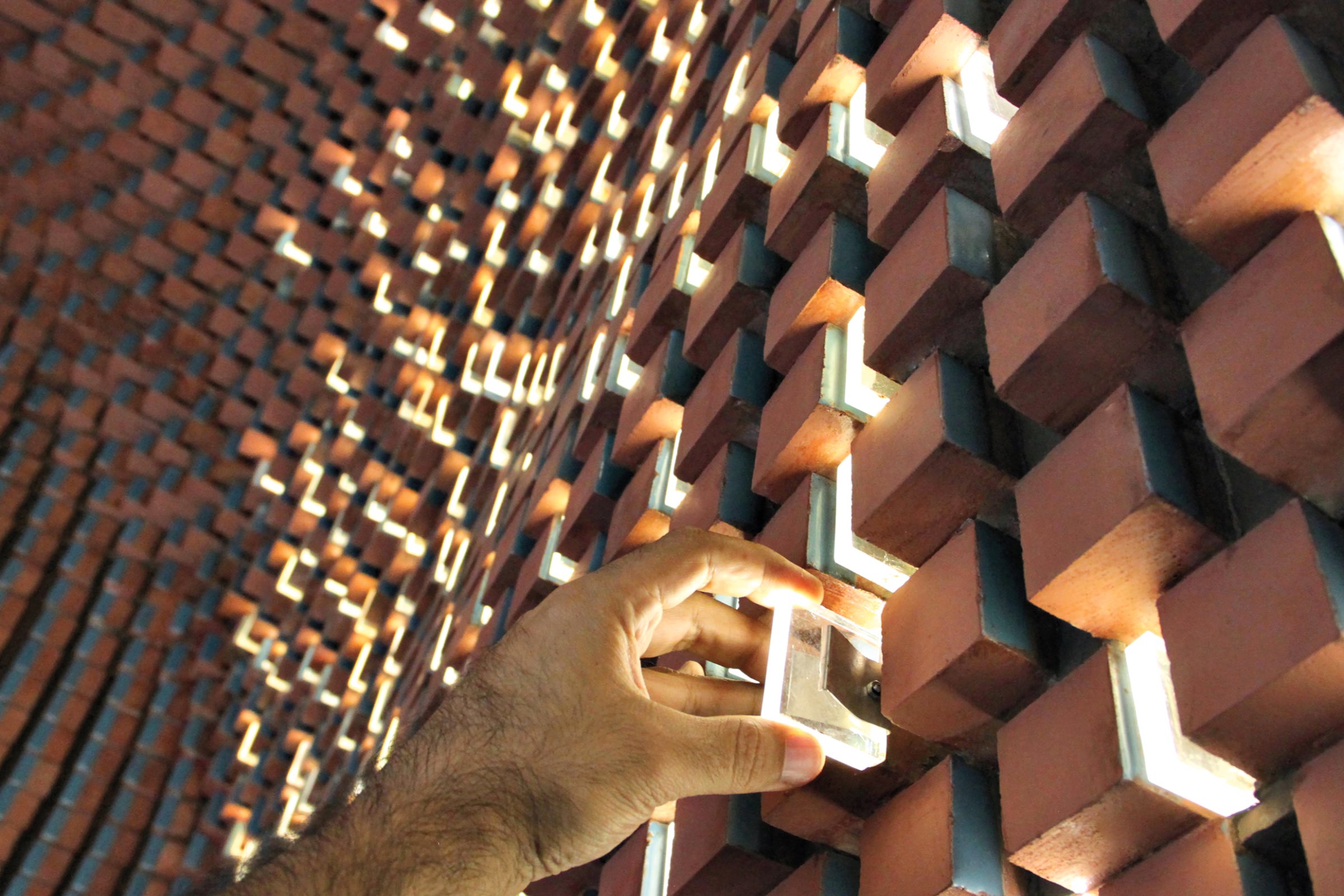 A hand adjusts a movable brick in a wall with a geometric pattern, allowing light to pass through rectangular openings.