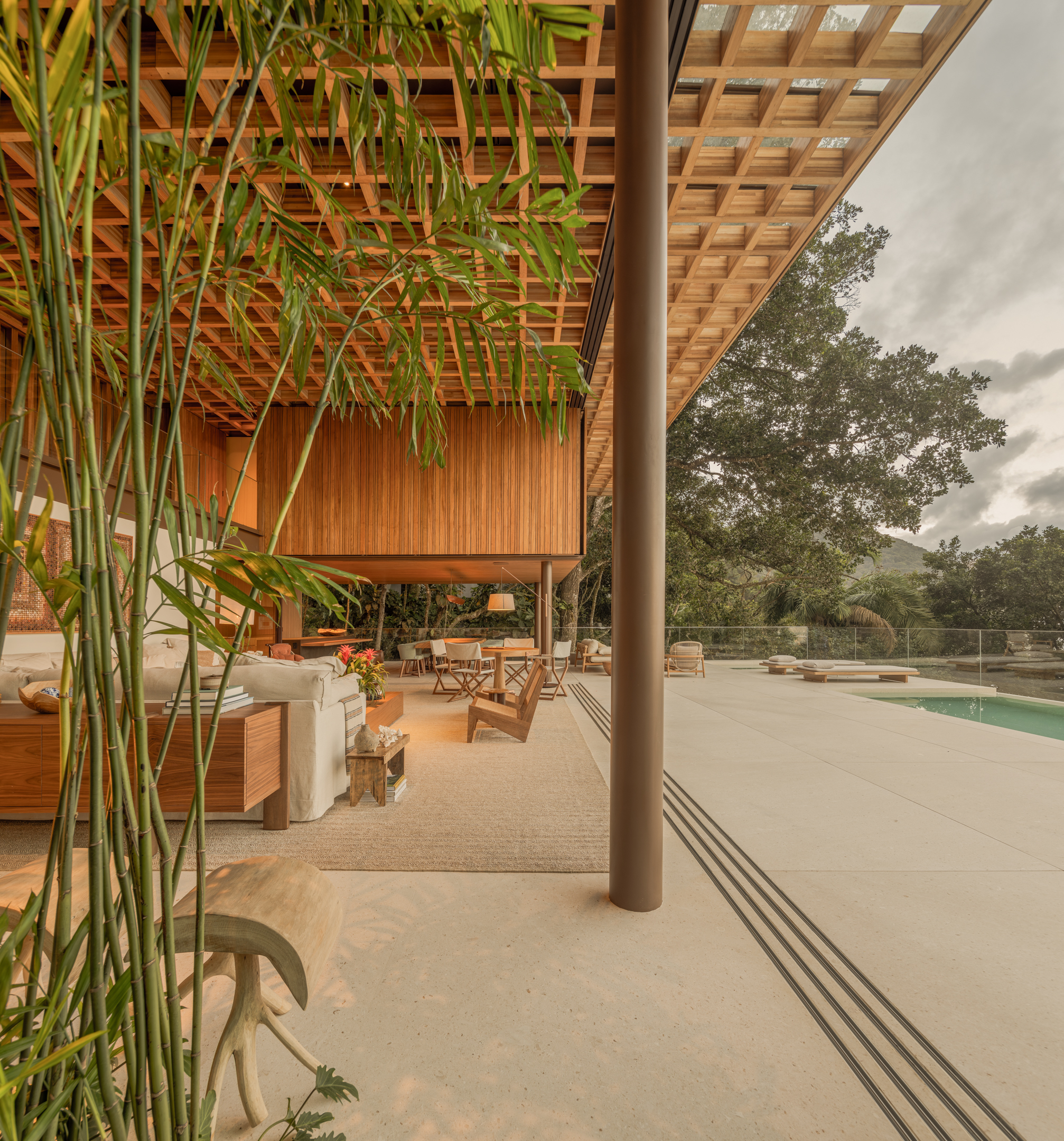 Modern open-air living space with wood ceiling, indoor plants, neutral furniture, and outdoor pool under a cloudy sky—designed with Passive House principles for optimal energy efficiency and comfort.