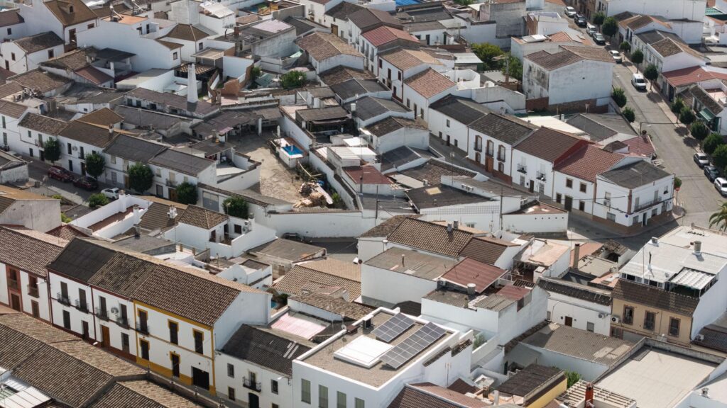 Aerial view of a neighborhood with closely packed white buildings, tiled roofs, narrow streets, and some solar panels visible—an area where the principles of Passive House design may be observed in the emphasis on energy efficiency and modern sustainability.