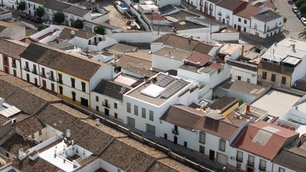 Aerial view of closely packed white buildings with brown tiled roofs in a residential area, featuring solar panels on one rooftop and showcasing thoughtful Passive House design principles for improved energy efficiency.