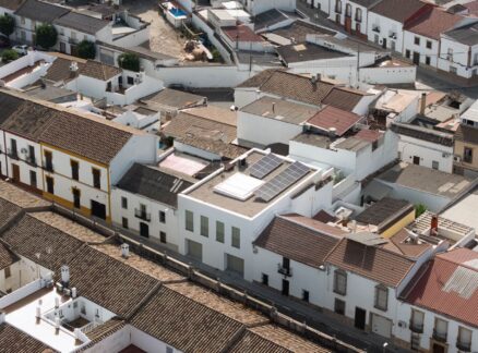 Aerial view of closely packed white buildings with brown tiled roofs in a residential area, featuring solar panels on one rooftop and showcasing thoughtful Passive House design principles for improved energy efficiency.