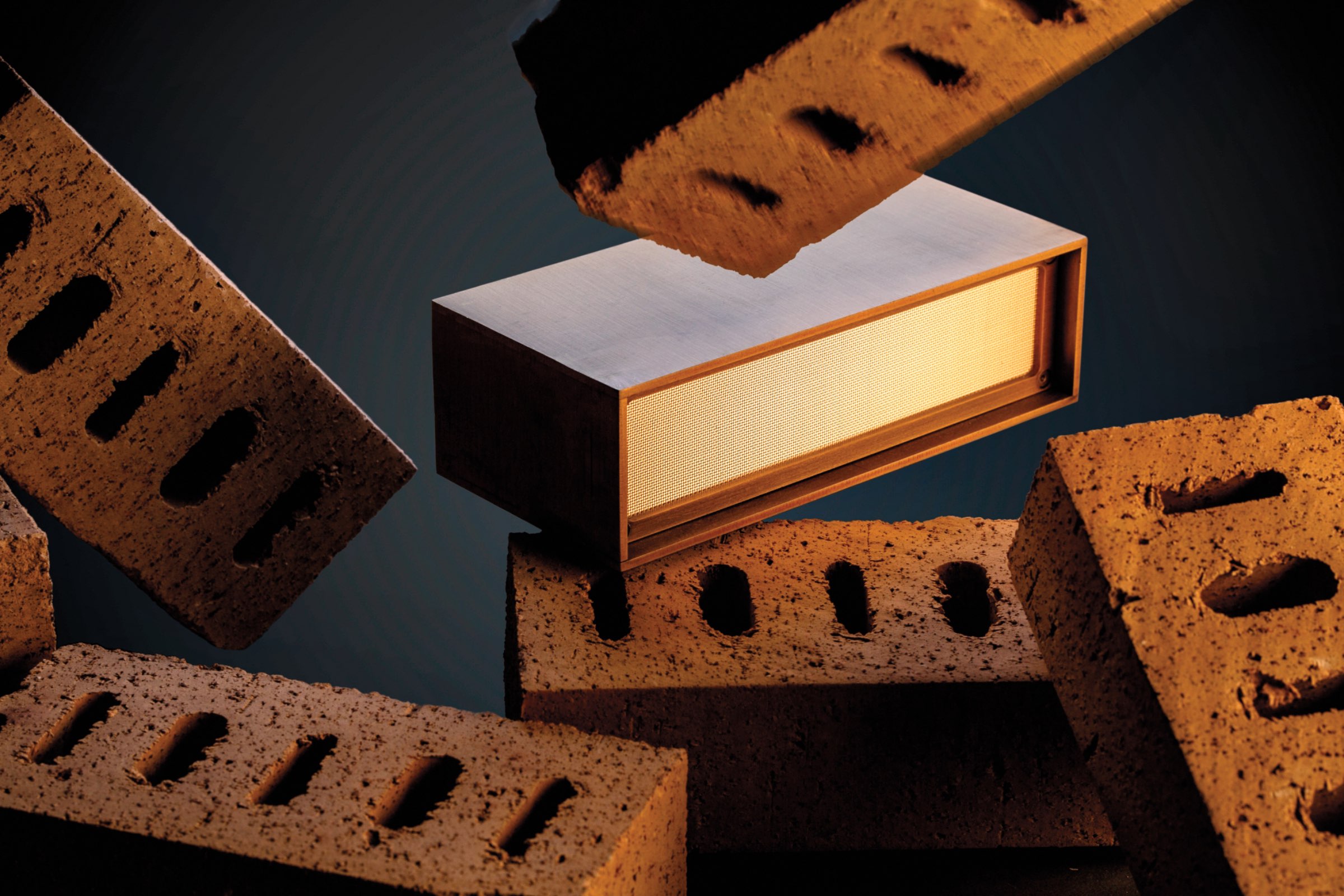 A rectangular speaker with a wooden frame sits among several brown bricks, some of which are stacked and others are suspended in midair.