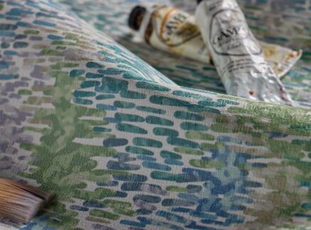 A paintbrush and two squeezed paint tubes rest on a textured, multicolored surface with blue, green, and lavender patterns, reminiscent of a Pallas-inspired palette.