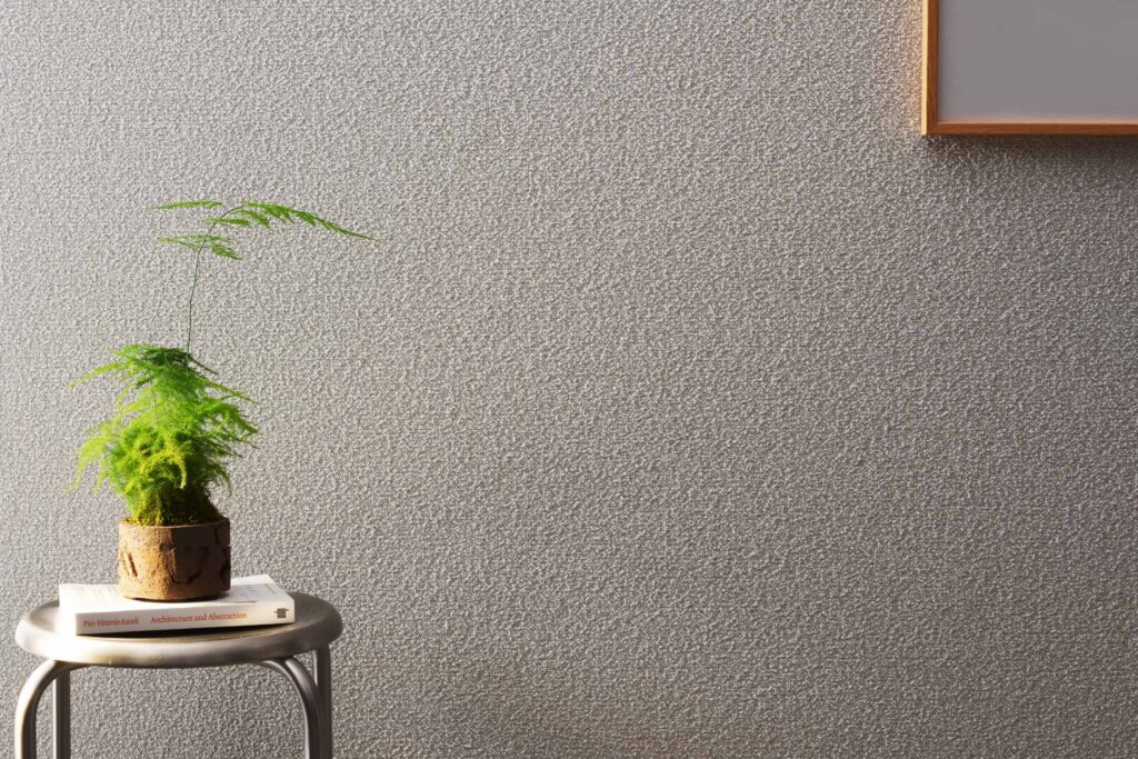 A small potted plant sits on a round metal table with two books, against a textured gray wall with a partial framed picture in the top right corner.