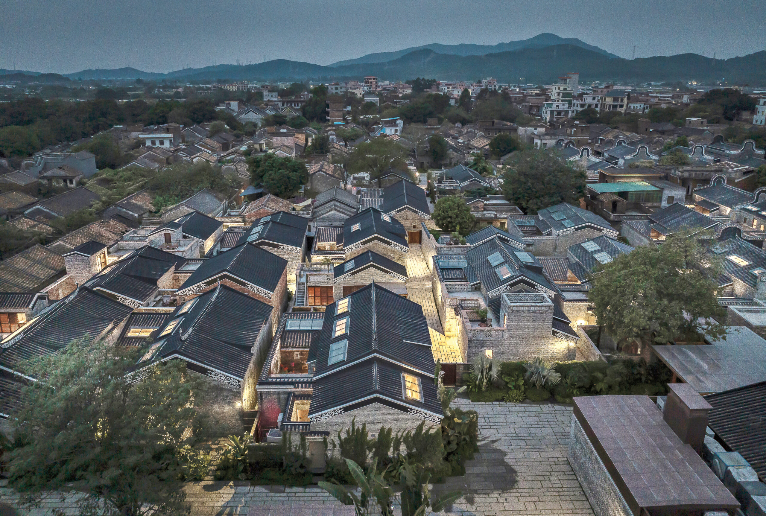 Studio Hu's Langtou Village Inn in Guangzhou, China shines with warm light in a skyline of rooftops from aerial view.