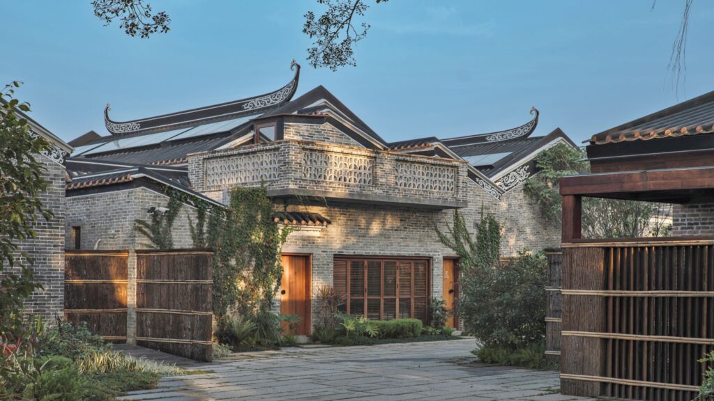 Studio Hu: Traditional Chinese brick building with ornate, upturned roof eaves, wooden doors, and a stone courtyard surrounded by greenery.