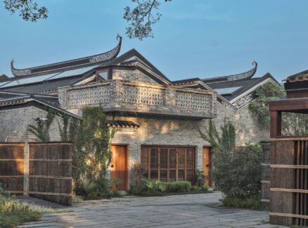 Studio Hu: Traditional Chinese brick building with ornate, upturned roof eaves, wooden doors, and a stone courtyard surrounded by greenery.
