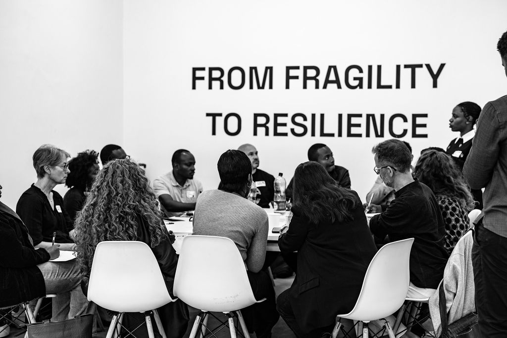 A group of people sit around a table in discussion; text on the wall behind them reads “FROM FRAGILITY TO RESILIENCE,” setting the tone for their inspiring conversation at UIA 2026 Barcelona.