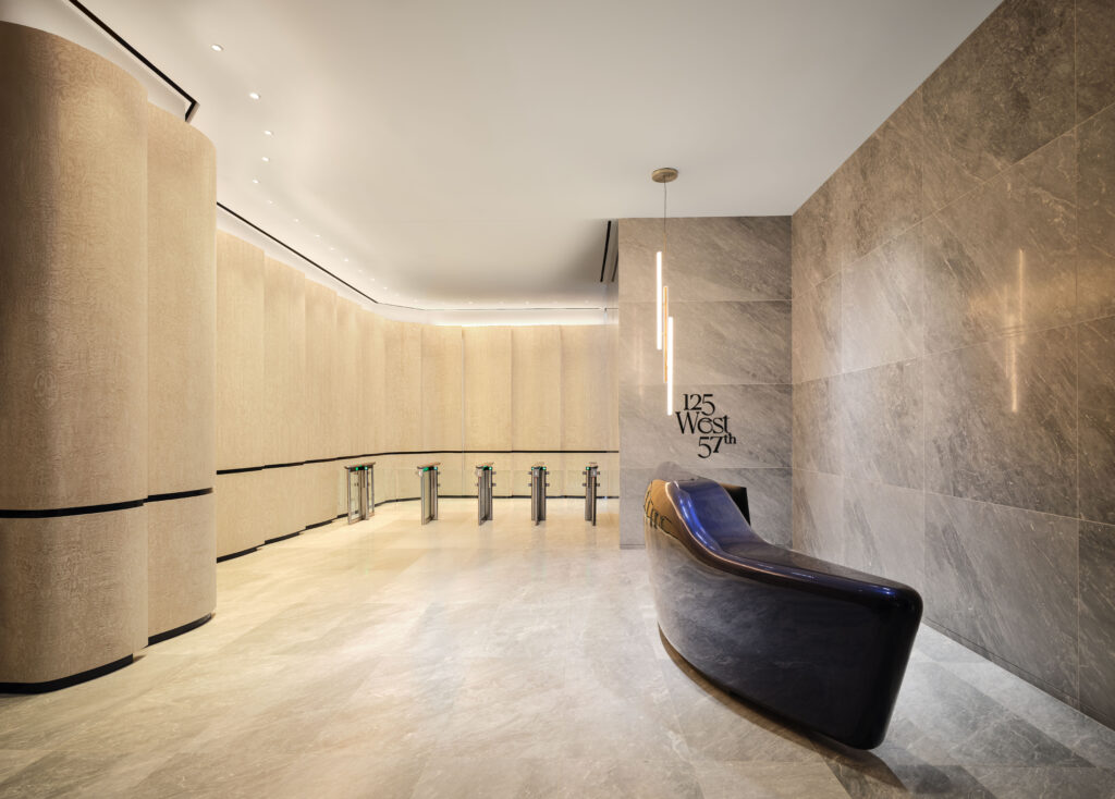 Modern building lobby with curved beige walls, stone flooring, a sleek black curved bench, security turnstiles, and “125 West 57” text on the wall. With its neutral color palette and minimal decor, the space draws inspiration from contemporary institutions like the Lucas Museum of Narrative Art.