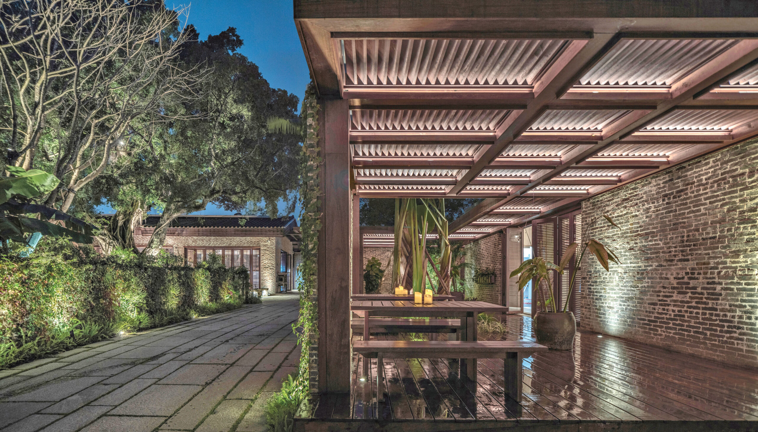 An indoor/outdoor living space in Langtou Village Inn by Studio Hu with green foliage and brick walls plus an outdoor seating area