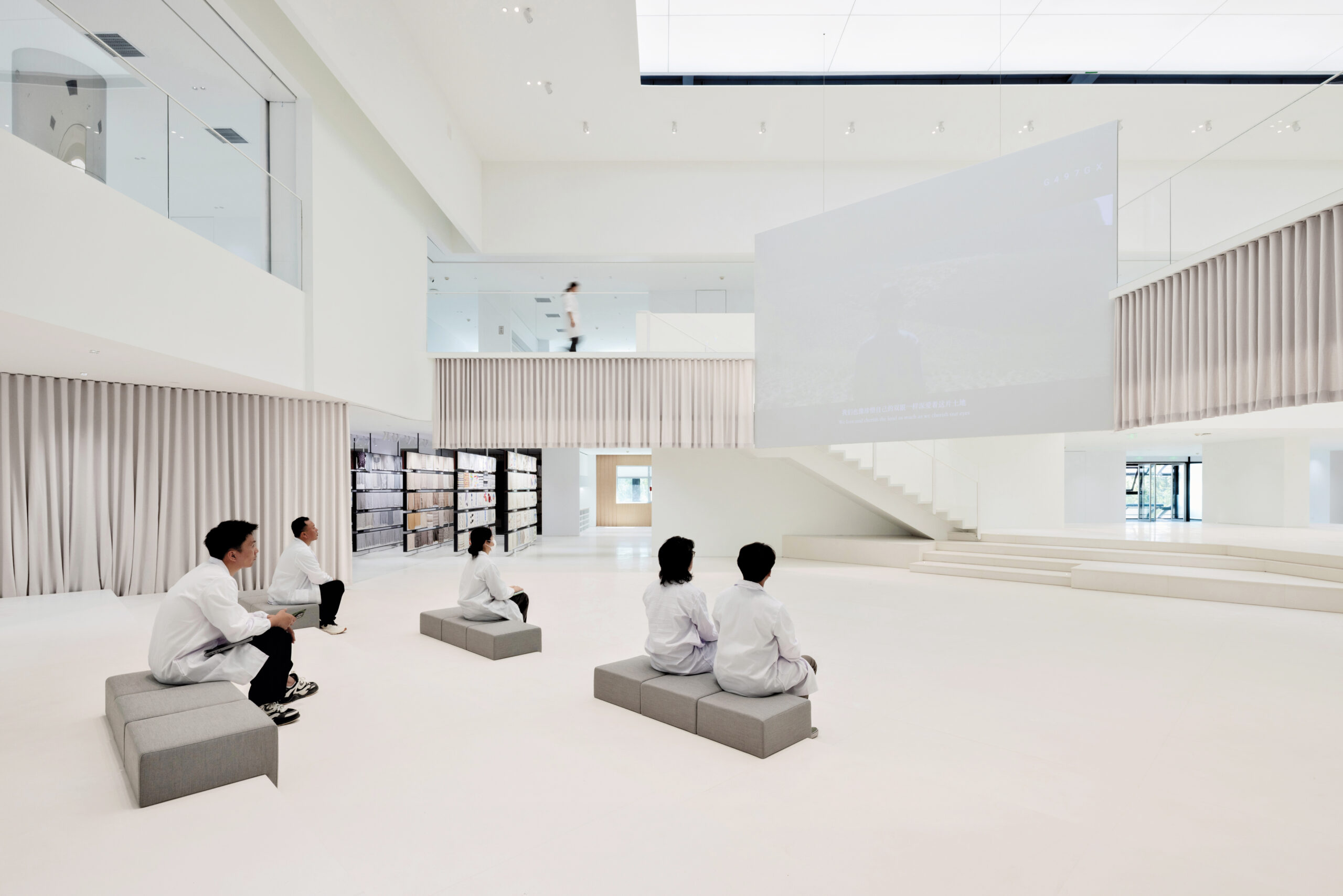 Inside the Erdos Cashmere Centre: white surfaces, staircases and drapery enclose a central ampitheatre, where five figures in white lab coats sit.